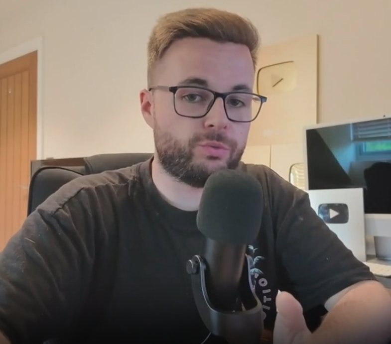 Jamie in the studio, speaking into a microphone in front of YouTube Play Buttons